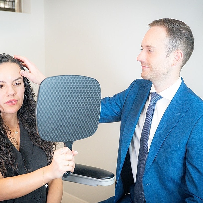 Stylist assisting client with hair in mirror.