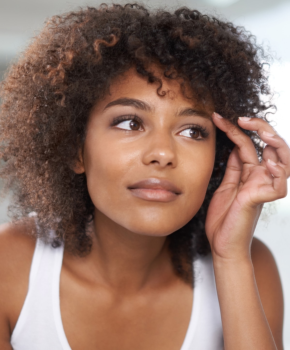 Young woman with curly hair looking thoughtfully upward.