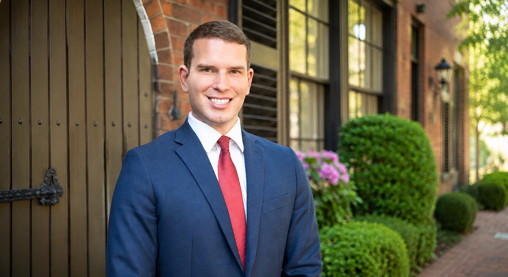 Smiling man in suit outside brick building.